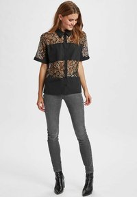 Zwarte short-sleeve shirt met ingewikkelde gouden kantpanelen, met een knoopsluiting aan de voorkant en een kraag. Gepaard met grijze skinny jeans en zwarte laarzen.