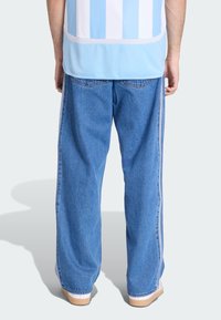 Pantaloni in denim azzurro chiaro con vestibilità ampia, caratterizzati da strisce laterali bianche, cuciture a contrasto e un leggero orlo sfrangiato ai polsini.