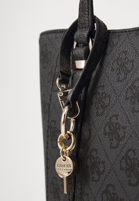 Sac à main synthétique noir avec une surface texturée et un motif en relief. Doté de quincaillerie dorée, d'un accessoire porte-clés et d'un design structuré.