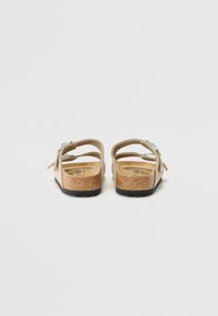 Sandales à semelle en liège en suede beige, avec un dos ouvert et des sangles ajustables en métal argenté. Semelle intérieure texturée pour le confort.