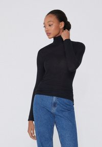 Schwarzer langärmeliger Rollkragenpullover aus elastischem Stoff, kombiniert mit blauen Jeans. Hat eine enganliegende Silhouette und eine glatte Textur.