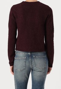 Vinröd stickad tröja med långa ärmar och rund halsringning, kombinerad med blå denimjeans med klassisk femficksdesign.