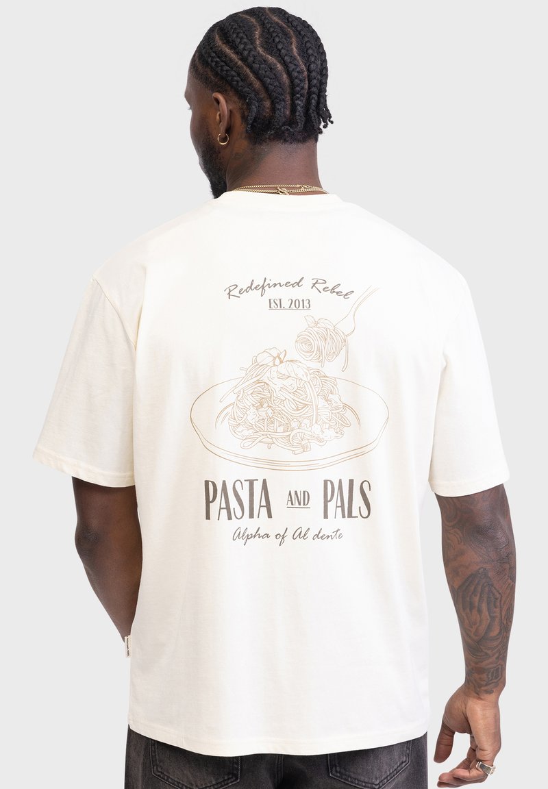 Flødefarvet bomulds-t-shirt med en pasta-grafik og tekstdesign på bagsiden. Indeholder "Redefined Rebel," "Pasta and Pals," samt detaljerede mønstre.