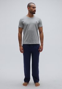 Pelēka īsroku krekls ar nelielu logotipu, saskaņots ar tumši zilām brīvā laika biksēm. Audums izskatās mīksts un ikdienišķs, piemērots ērtai valkāšanai.