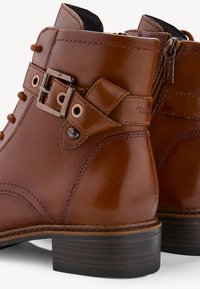 Bottines en cuir marron avec une finition légèrement brillante, fermeture éclair latérale et détail de boucle décoratif sur le dessus. Talon en bois.