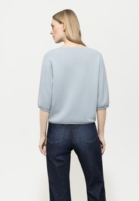 Hellblauer, strukturierter Pullover mit halbarmigen Ärmeln, getragen mit dunklen, hoch taillierten, geraden Jeans. Einfaches Design, keine Muster.