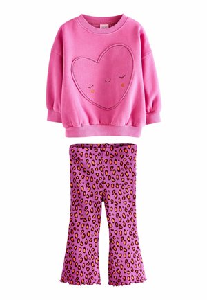 Rosa sweatshirt med ett hjärtmönster och ett leende ansikte, kombinerad med lila utsvängda leggings med ett svart och orange leopardtryck.