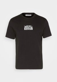 Camiseta de algodón negra con mangas cortas y cuello redondo. Presenta un logo "Calvin Klein" impreso en blanco dentro de un diseño rectangular.