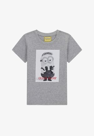T-shirt gris à manches courtes avec un personnage Minion portant des gants noirs et une salopette imprimés sur le devant, avec le texte "GUESS JEANS" en dessous.