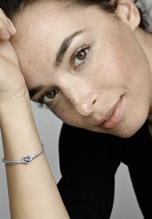Bracciale d'argento con design a nodo infinito. Presenta una catena texture e superfici lisce, su uno sfondo neutro.