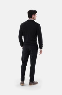 Dunkelgrauer Pullover mit Schalkragen, kombiniert mit schmalen schwarzen Hosen und grauen Wildleder-Ankle-Boots, von hinten betrachtet.