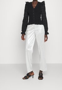 Schwarzer Strickpullover mit Eyelet-ÄrmelDetails, kombiniert mit silbernen, metallischen weit geschnittenen Hosen und schwarzen, rückenfreien Absätzen mit Rüschendetails.