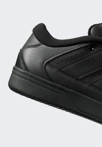 Černá nízká teniska s texturovanou podrážkou, polstrovaným límcem a perforovanými bočními panely na jednoduchém světlém pozadí.