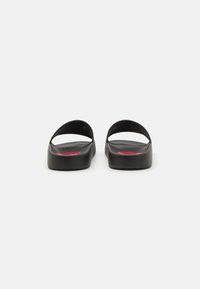 Black slide sandals with a textured surface, open design, and a subtle red accent on the footbed. Rounded strap above the foot.