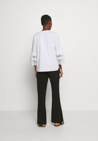 Blusa blanca con mangas acampanadas de encaje, combinada con pantalones negros de campana. La blusa tiene un escote redondo y una textura suave.