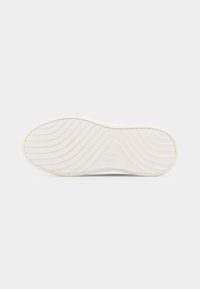 Semelle de chaussure blanche avec des rainures courbes et diagonales pour l'adhérence, comportant un petit logo en relief au centre, isolée sur un fond clair.