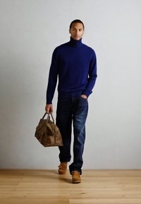 Marinefarbener Rollkragenpullover, Jeans, beige Schuhe und eine braune Tasche. Stylisches, figurbetontes Design, glatte Textur und kontrastierende Farben.