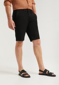 Svarta denimshorts med regular fit, med framfickor och en ren finish. Matchas med svarta platta sandalskor med korsade remmar.