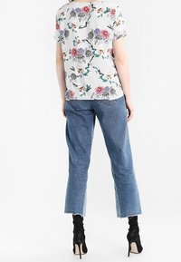 Floral-patterned white blouse with short sleeves, worn with blue denim cropped jeans and black heeled ankle boots.