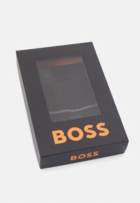 Confezione nera con una finestra trasparente che mostra un oggetto nero all'interno. "BOSS" stampato in grassetto arancione sul davanti e sul lato.