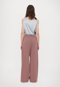 Satin lys blå uten ermer topp med en subtil drapering, paret med vide ben, pastell rosa bukser med en glatt tekstur og elastisk midjebånd.