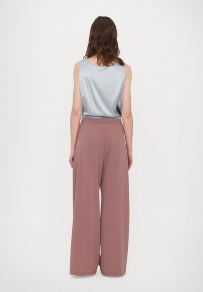 Top senza maniche in satin blu chiaro con un drappeggio sottile, abbinato a pantaloni a gamba larga in un delicato rosa pastello con una texture liscia e una cintura elastica.