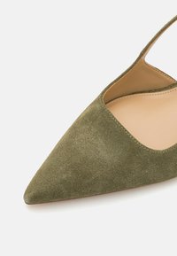 Green suede pointed-toe shoe with an open heel and side cutout, featuring a smooth inner lining and a minimalist design.