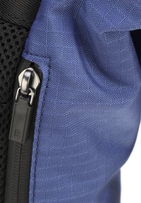 Borsa in tessuto blu con superficie testurizzata. Presenta una zip nera e bordino in rete. Prima di una chiusura che mostra i dettagli della cucitura e della zip.