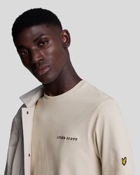Bežinė medvilninė marškinė su juodu siuvinėtu "LYLE & SCOTT" užrašu, o kairiajame rankovėje – geltonas siuvinėtas logo. Kasdienis dizainas.