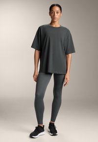 Tricou supradimensionat de culoare gri închis, din material moale, asortat cu colanți gri închis cu talie înaltă și pantofi sport negri. Design minimalist.