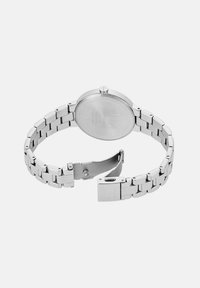 Hõbedane metallist käekell avatud klapiga, mis näitab tagakaant ja linkide käevõru riba lihtsal taustal.