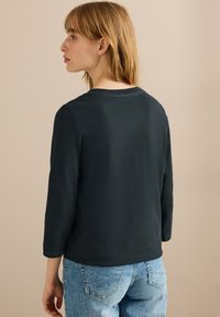 Mörkblå långärmad topp med rund halsringning, mjuk textur och avslappnad passform, kombinerad med ljusblå denimjeans.