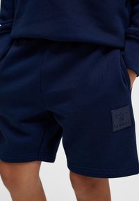 Navyblauwe shorts van zachte stof, met een elastische tailleband, twee zijzakken en een verhoogd logopatch op de linker bovenbeen.
