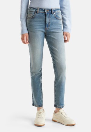 Jean taille haute bleu clair avec un délavage, design à jambe droite, poches avant et détails de couture subtils, associés à des baskets blanches.