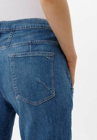 Jeans de mezclilla azul desgastados con un bolsillo trasero con costura en triángulo y botón de metal. Textura suave con un diseño de pierna recta.