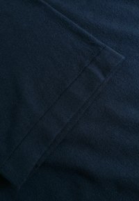 Gros plan sur un tissu bleu foncé montrant une couture pliée avec des coutures visibles et une texture douce.