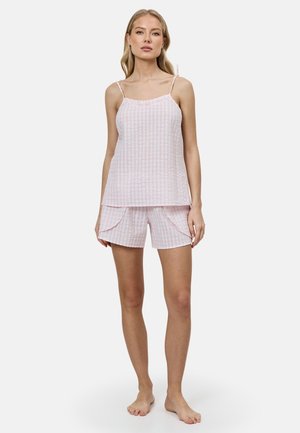 Vrouw draagt een lichtroze geruit mouwloos topje met dunne bandjes en bijpassende shorts met gelaagde ruches, staat blootsvoets.