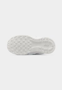 Λευκή σόλα παπουτσιού Nike με ανάγλυφα τετράγωνα και κυκλικά πέλματα, και ανάγλυφο το λογότυπο "NIKE" κοντά στη φτέρνα, σε απλό ανοιχτό γκρι φόντο.
