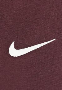 Maroon kangas yenye muundo wa kutofautisha ina alama ya Nike ya rangi nyeupe, iliyoshonwa na kuwekwa katikati ya nyenzo.