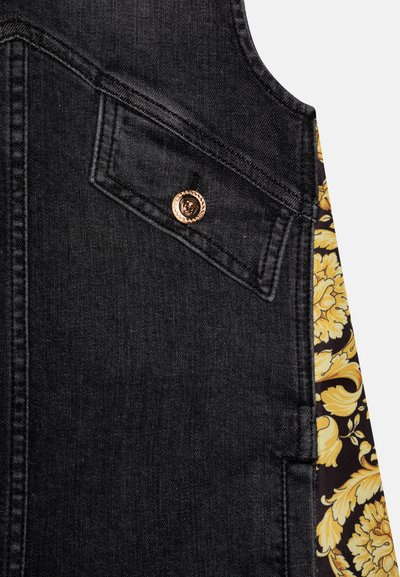 Oddelek iz črnega jeans blaga z nagnjenim žepom z zaponko v obliki zlatega Meduzinega obraza, obdan s črno in rumeno cvetličasto karirano tkanino.
