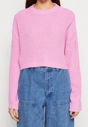 Pull court en tricot rose avec un motif texturé et des manches longues, associé à un pantalon en denim taille haute avec de grandes poches.