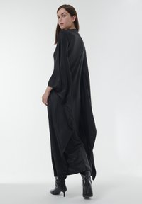 Zwarte, lange, vloeiende jurk met brede mouwen en een gedrapeerd ontwerp. Gladde, glanzende textuur; minimalistisch met een moderne silhouet.