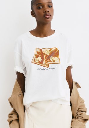 T-shirt blanc en coton avec une illustration de deux tranches de pain grillé avec du beurre et un texte manuscrit disant « Pas sans mon petit-déjeuner. »