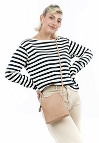 Torebka typu crossbody w kolorze tan, wykonana z gładkiej skóry, z zakrzywionym zamkiem na górze i pojedynczym regulowanym paskiem. Modelka nosi bluzkę w paski.