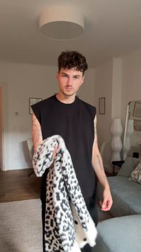 Camisola preta sem mangas, segurando uma manta com estampado de leopardo preto e branco. Textura suave, com padrões ousados e contrastantes. Ambiente interior.