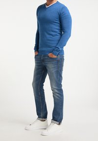 Pullover blu a scollo a V realizzato in materiale a maglia, abbinato a jeans azzurri. Le calzature sono sneakers bianche con lacci e senza motivi visibili.