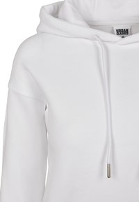 Vit huvtröja gjord av mjuk bomull, med en stor huva, dragsko med metallspets och avslappnad halslinje. Minimalistisk design utan mönster.