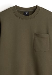 Olijfgroene sweatshirt met ronde hals, gemaakt van een zachte katoenmix. Heeft een enkele borstzak met een ronde onderkant en gestikte rand.