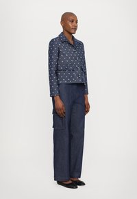 Marineblauwe cropped jas met een klein bloemenpatroon, twee knopen en voorzakken, gecombineerd met losse donkere denimbroek en zwarte ballerina's.