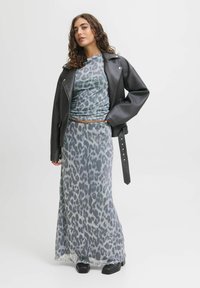 Abito senza maniche con stampa leopardata in tessuto grigio trasparente, abbinato a un giubbotto oversize in pelle nera e stivali neri chunky.